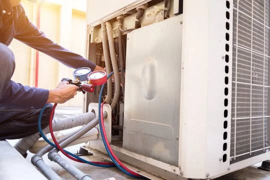 Technician checking refrigerant pressure with gauges on an outdoor AC unit