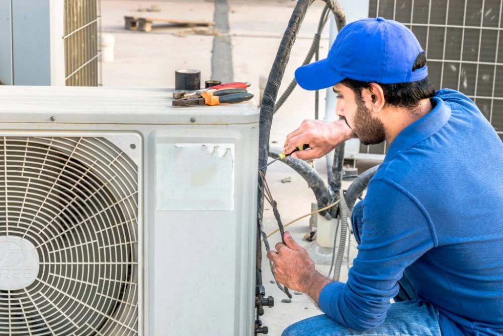Technician in blue workwear servicing an outdoor air conditioning unit